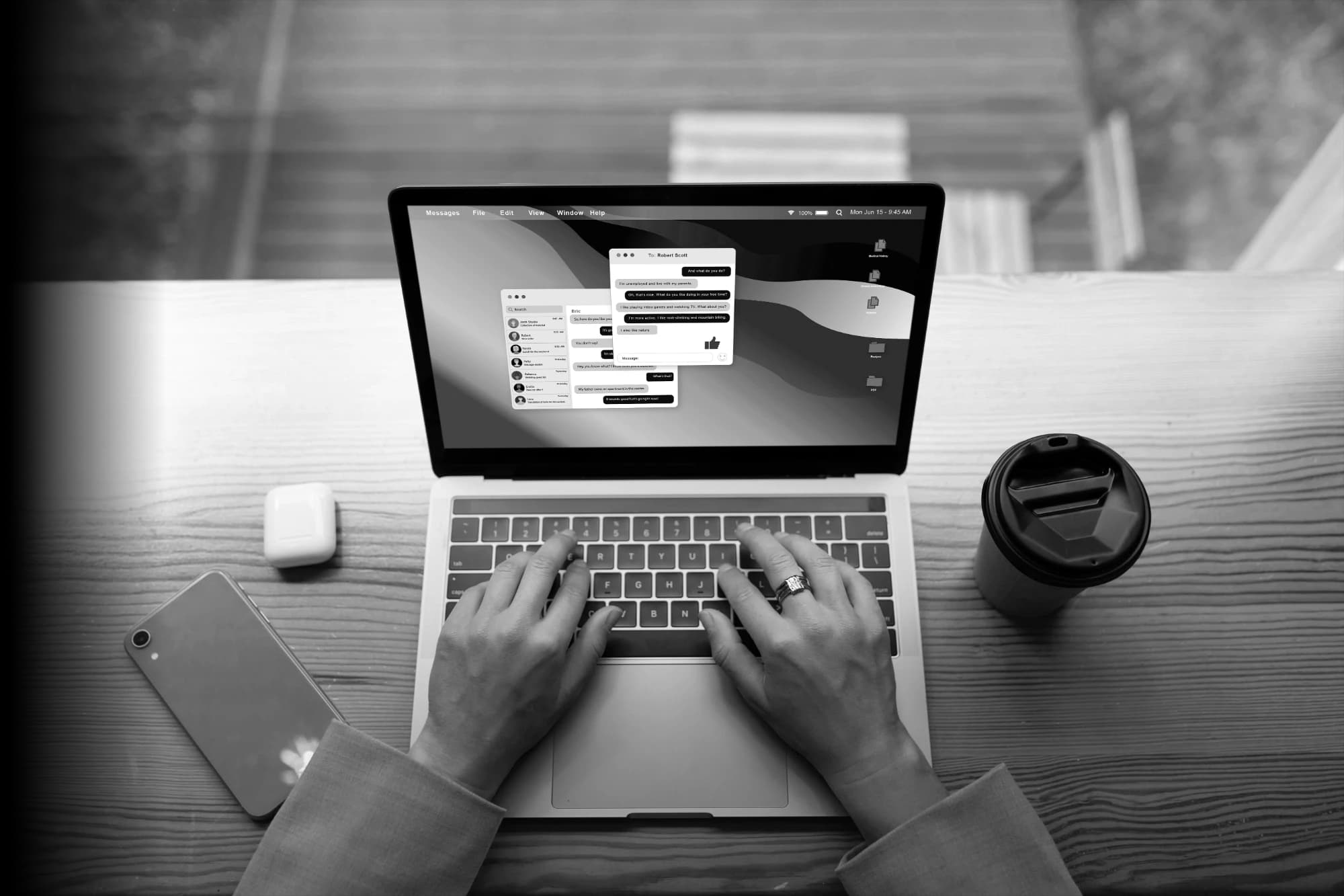 Overhead view of hands typing on a laptop showing a messaging app, beside a phone, earbuds and a coffee cup