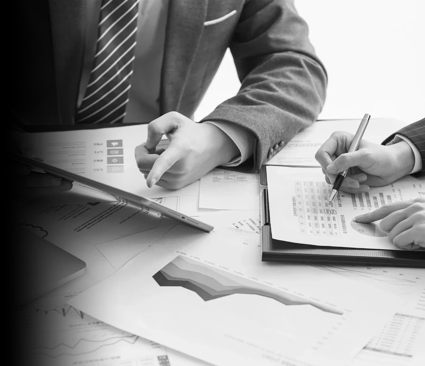 Colleagues in business attire review printed financial charts and reports with a tablet and laptop